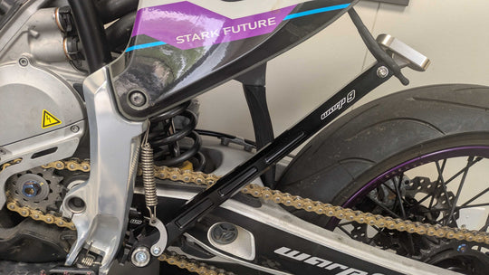 Warp 9 adjustable kickstand in black installed on a Stark Varg, folded up under the swingarm beside the chain
